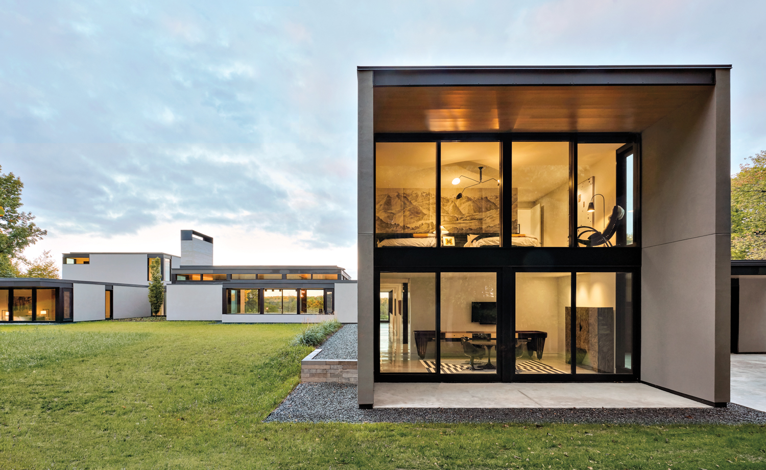 The outside of a modern stucco house with black-frame floor-to-ceiling windows.