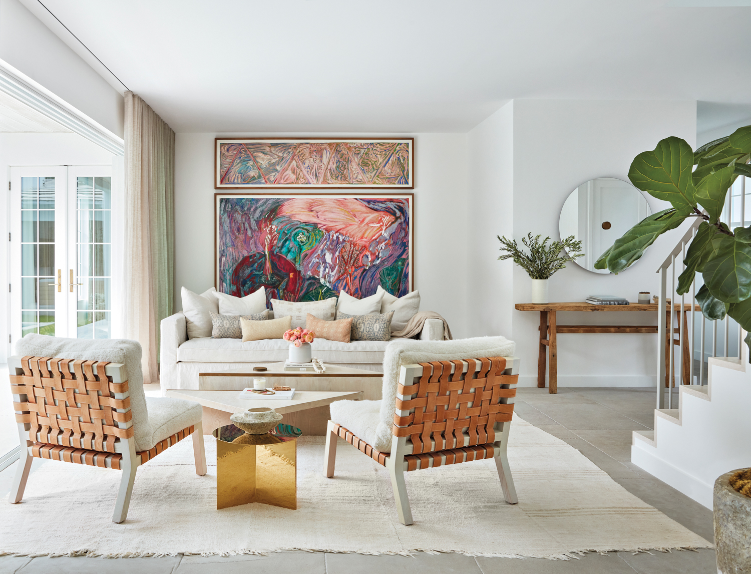 living area with white rug, white armchairs, white sofa, gold coffee table and colorful artworks