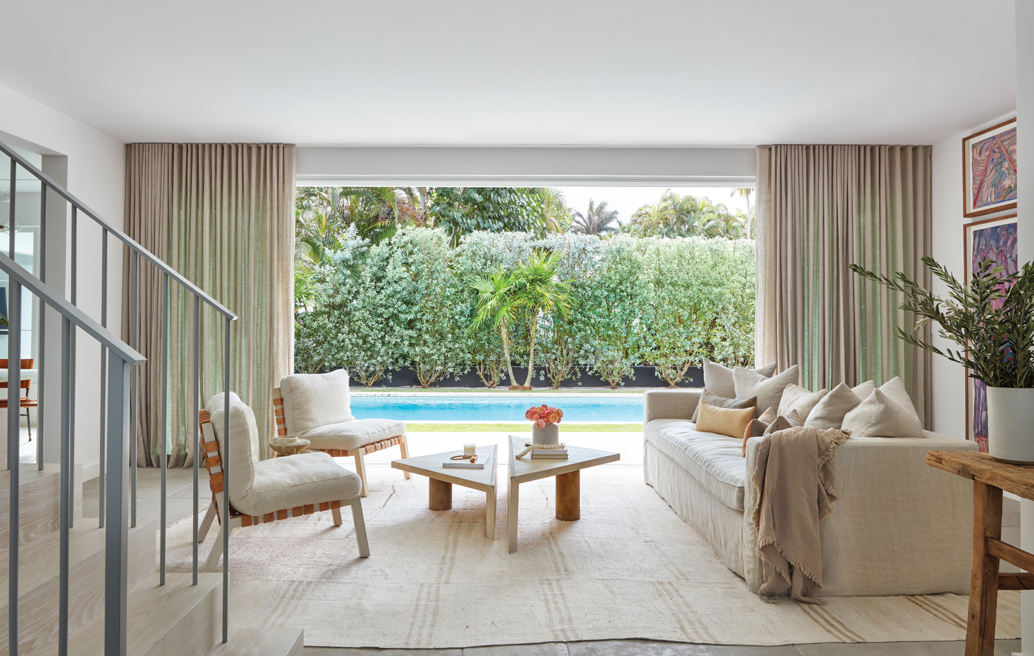 living area with white armchairs, neutral sofa and draperies, triangular coffee tables and pool view