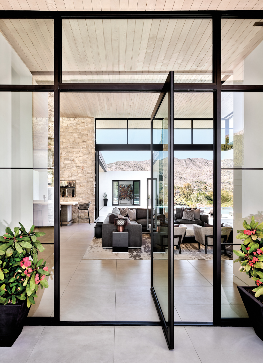 An entry way into the house with glass-and-steel doors. Past the living room you can see through the backyard with a mountain in the background.