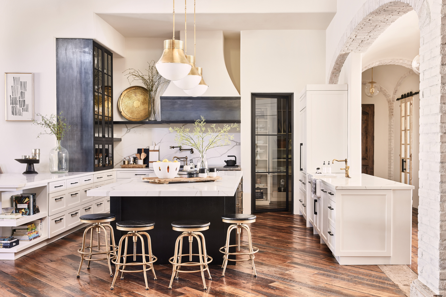 A kitchen with white cabinetry and a a marble-topped island with a black base. Four black-and-brass stools are at end of the island.