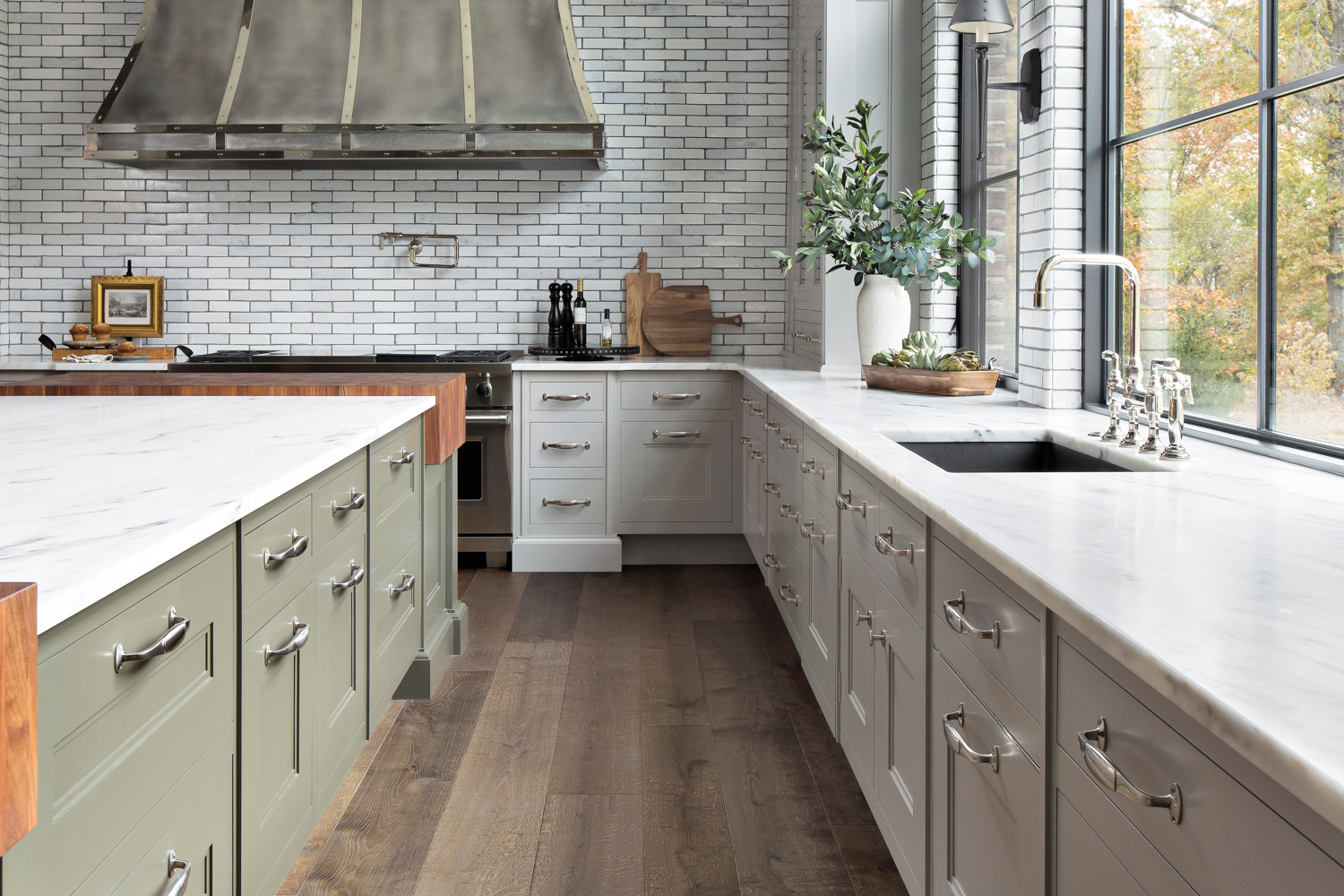 sage green kitchen cabinets with statement metal range hood and tile backsplash