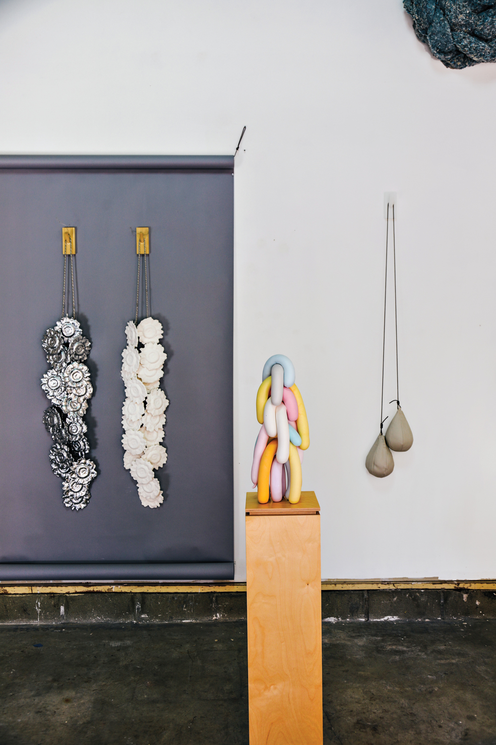 cast floral objects hung on wall beside sculpture of stacked cast balloons