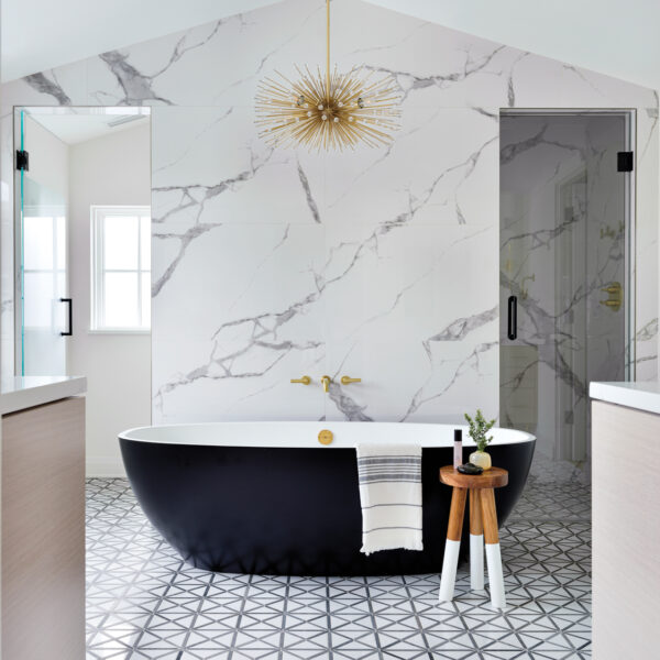 L.A. Style Sets The Stage For A Chicago Couple’s Dream Home A the center of a bathroom is a black bathtub in front of a gray-and-white porcelain feature wall.