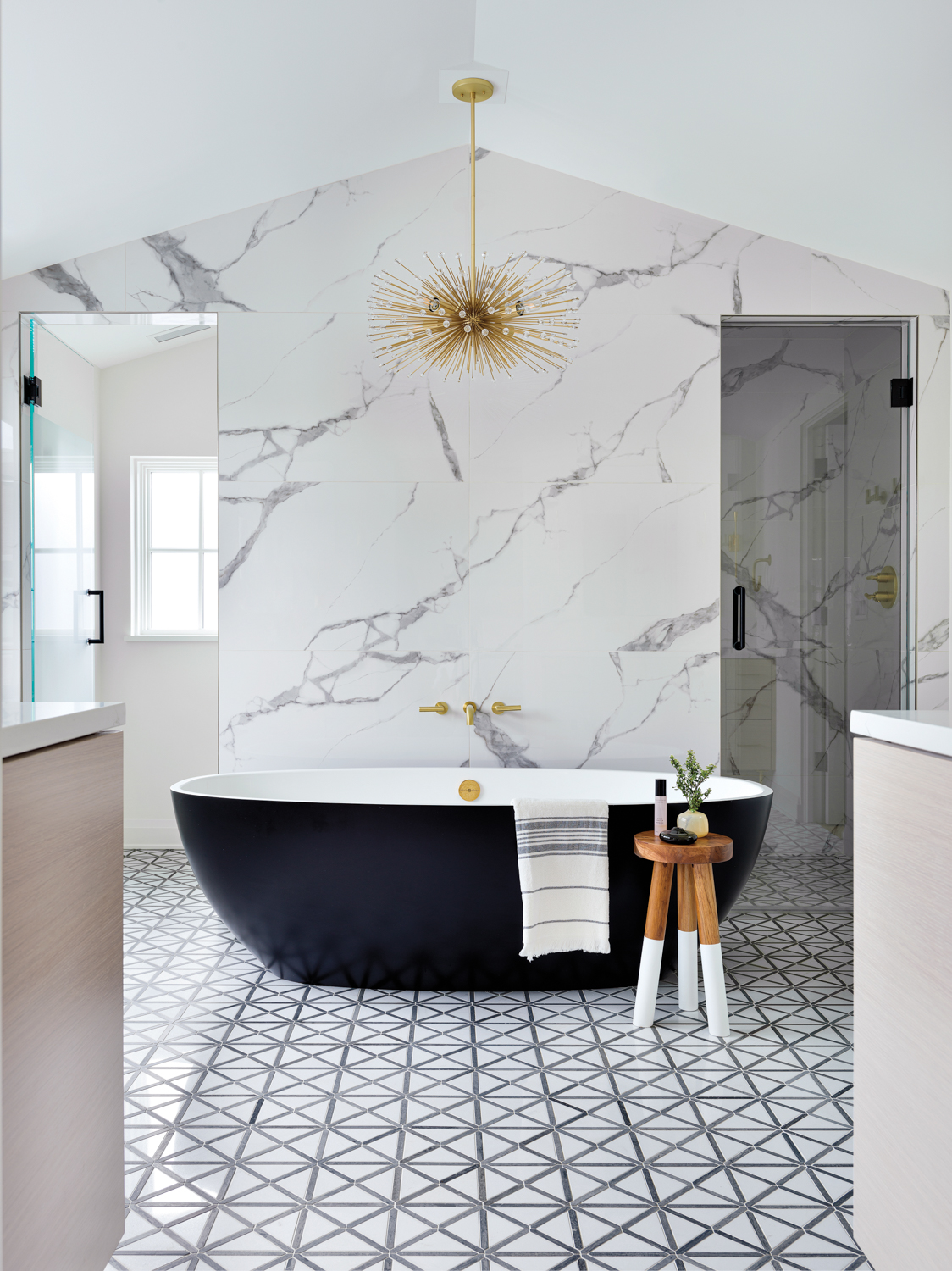 A the center of a bathroom is a black bathtub in front of a gray-and-white porcelain feature wall.