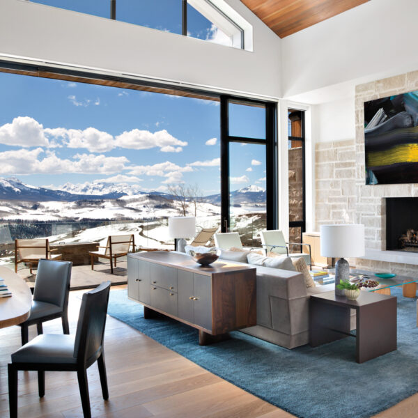 contemporary living room with open sliders to mountainous landscape, with fireplace, couch and deck area