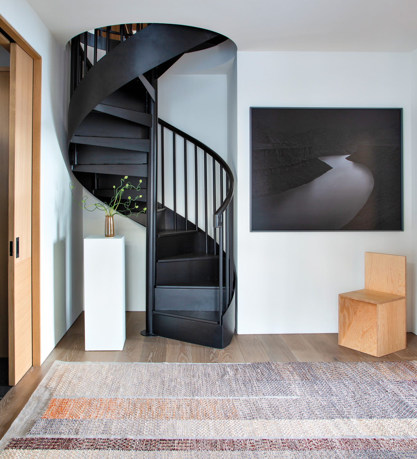 entryway with black spiral staircase leading to library loft and framed photograph on wall