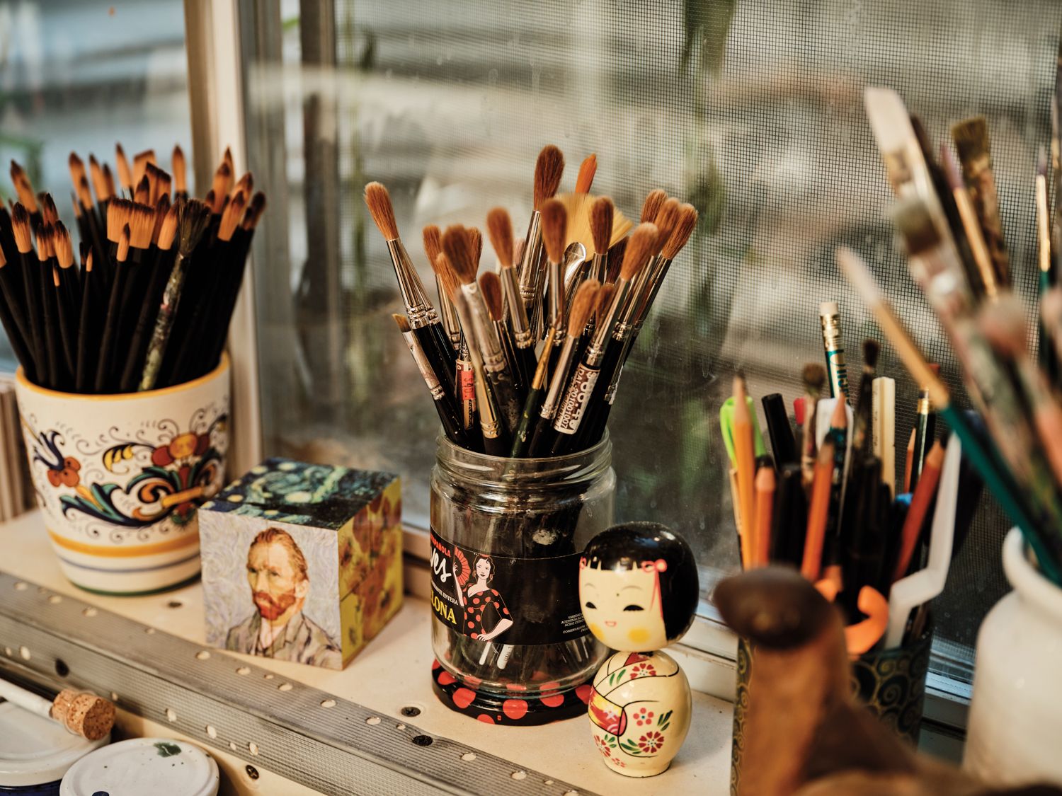 vignette of paintbrushes in jars and cups with figurines alongside