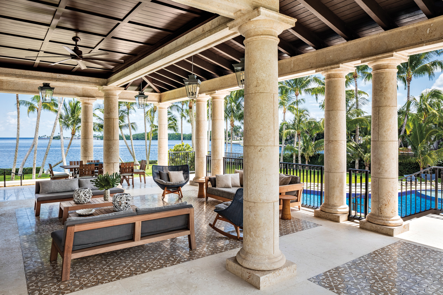 covered balcony with coral stone columns, seating area and dining area overlooking pool and water