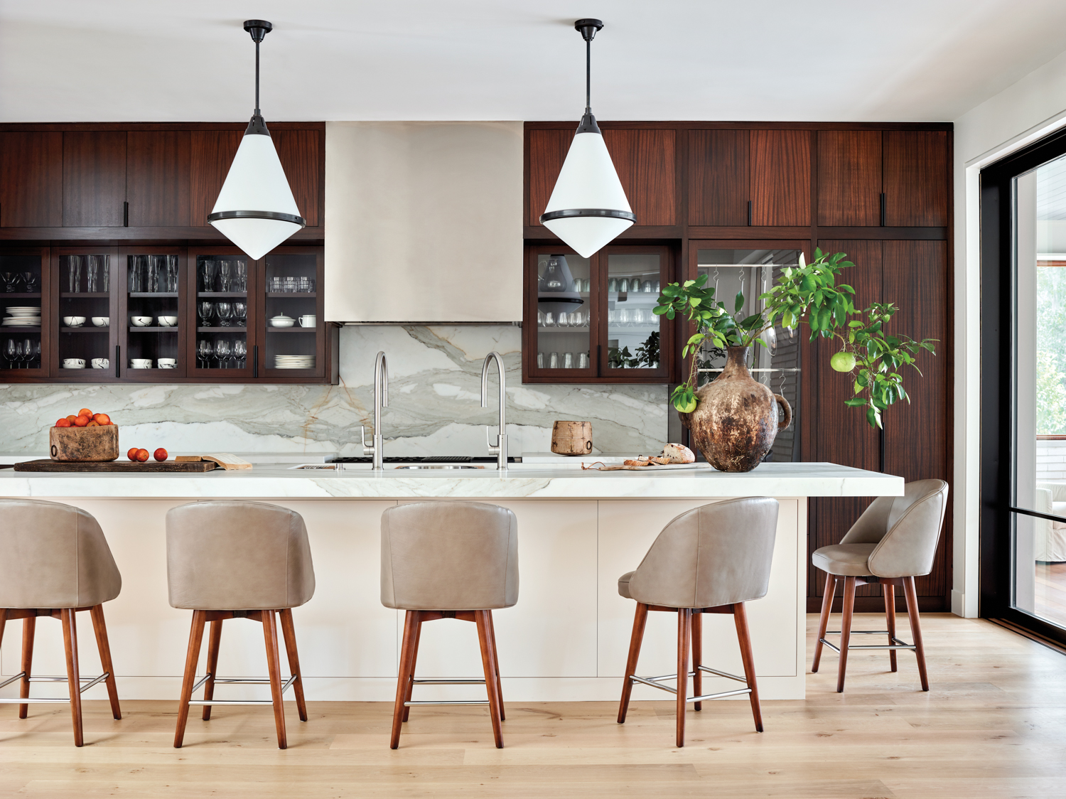 Kitchen with leather counter stools, white pendant lights and rich-toned wood cabinetry