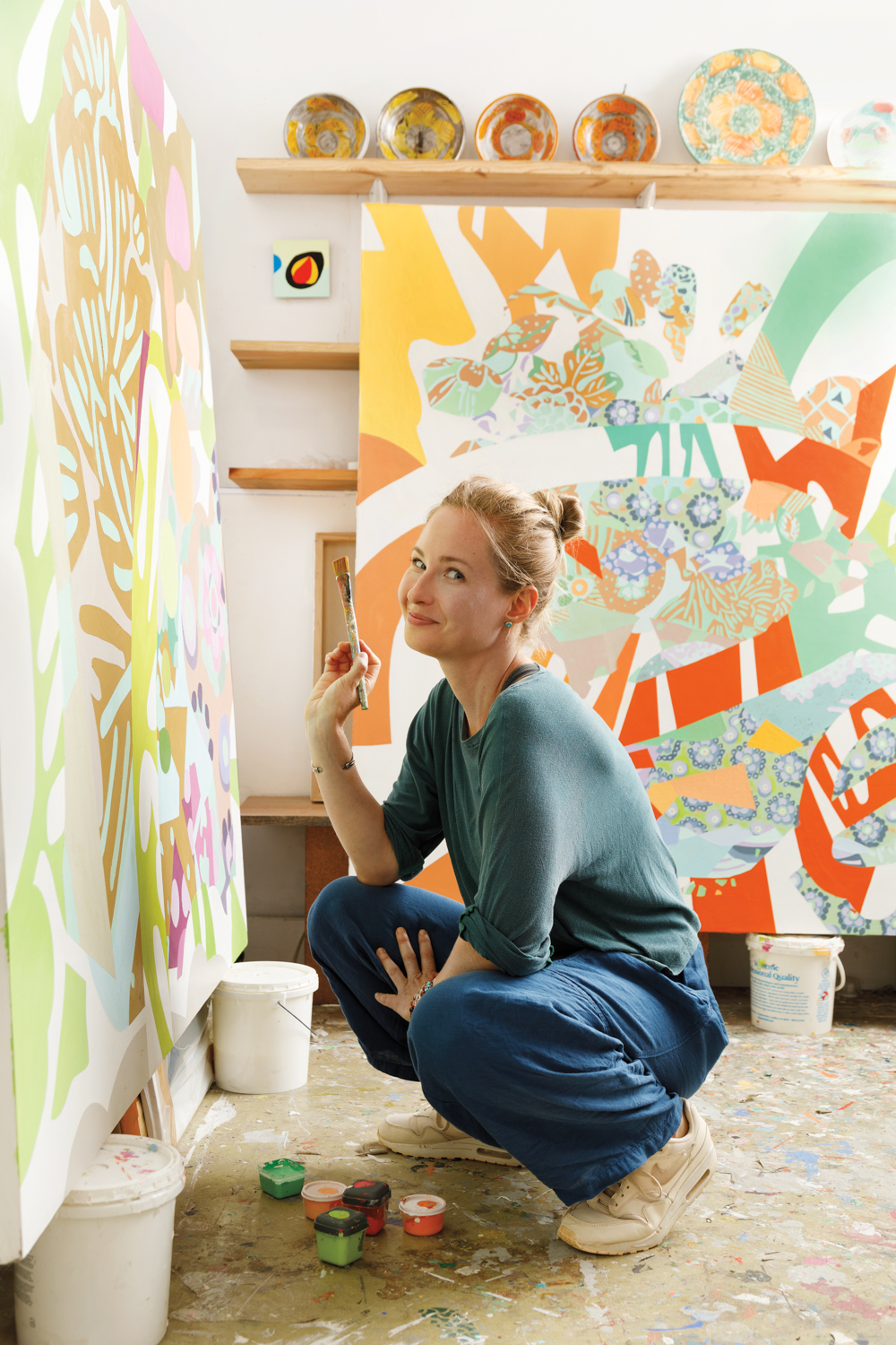 Woman holding a paintbrush crouching down before a colorful abstract painting