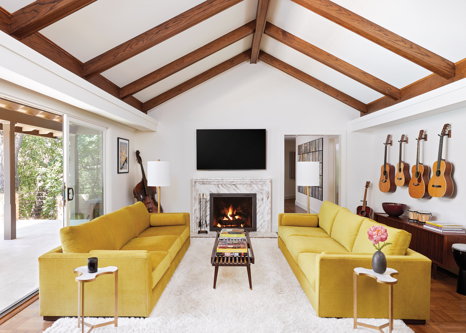 Living room with vaulted ceiling and beams and a pair of yellow sofas flanking a marble mantel