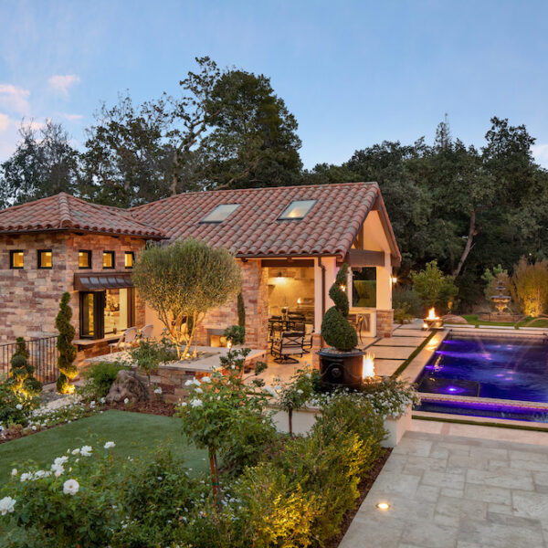 exterior of a pool house of a Northern California home with infinity edge pool, outdoor seating and a wrought iron fence by De Mattei Construction