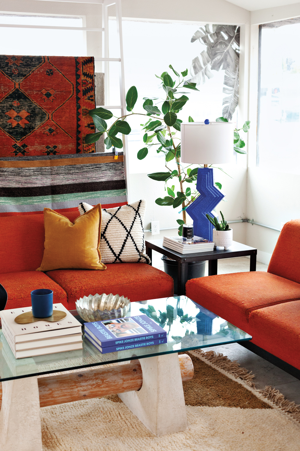 Seating vignette in store with orange sofas, hanging rugs and blue lamp.
