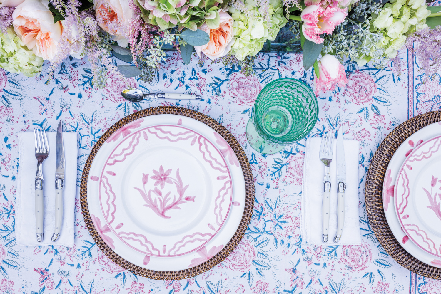 designer Constanza Collarte outdoor table set with pink plates, florals tablecloth and green glasses