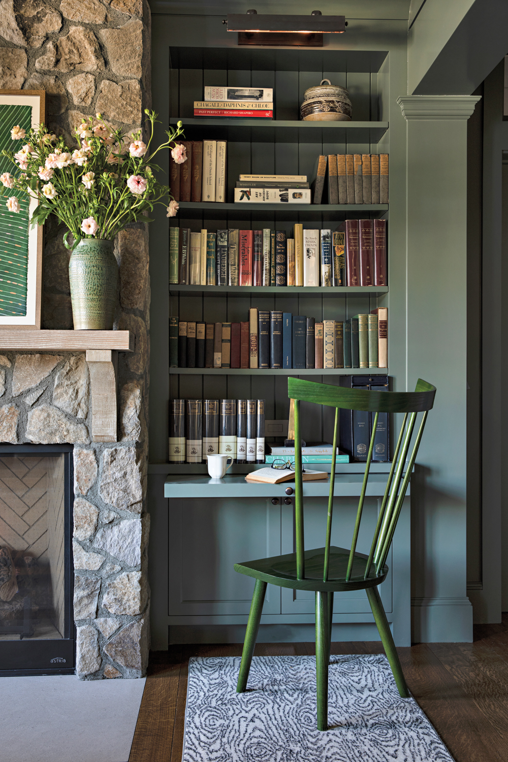 gray green library nook with green chair next to stone fireplace 