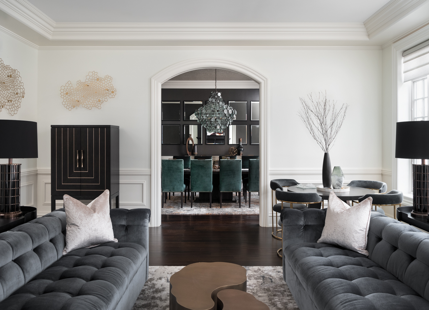 The view into a dark dining room from a living room with two gray velvet couches.