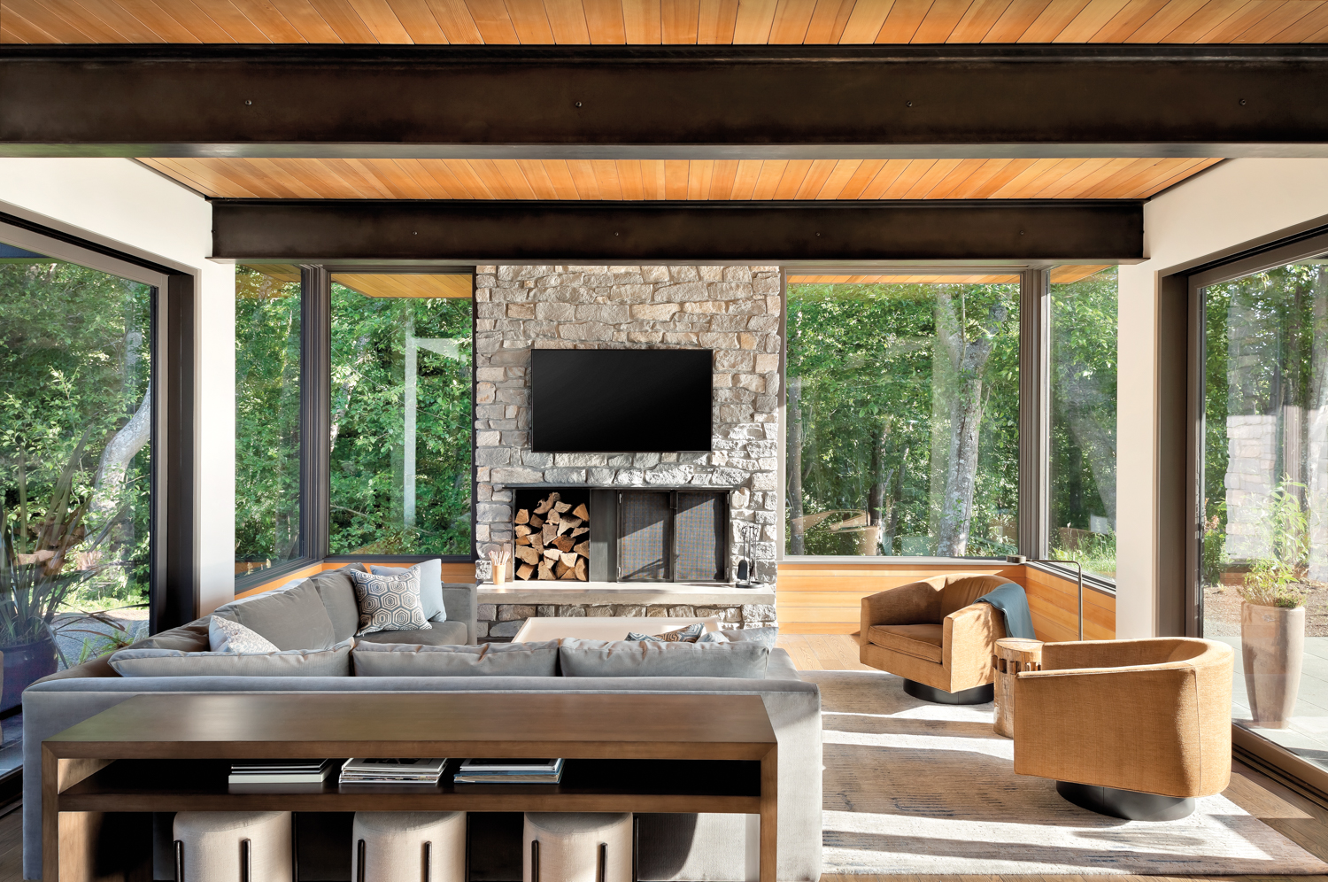 A living room is surrounded by windows and has a centrally located stone fireplace.