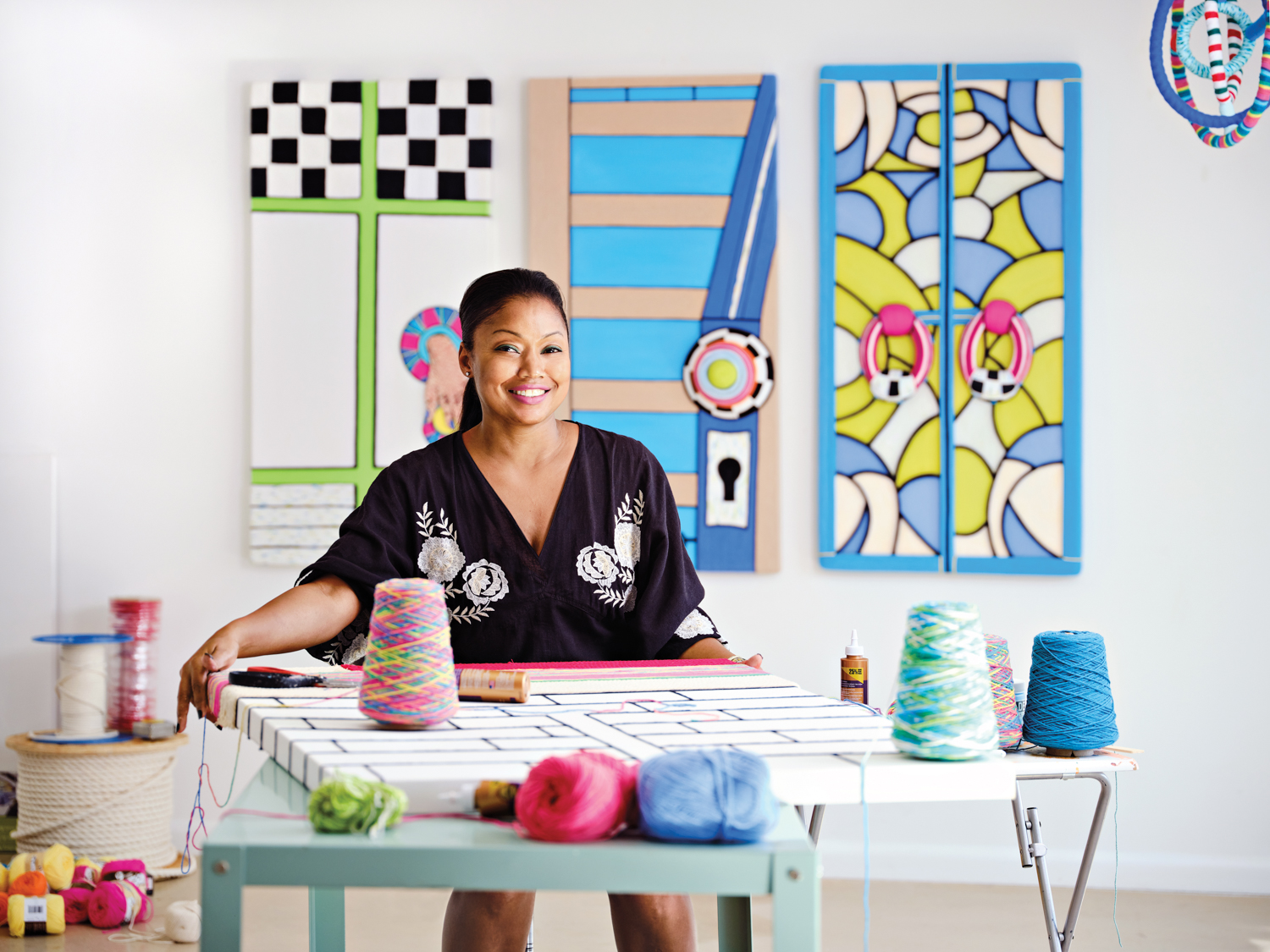 artist michelle drummond at a table of yarn with her three-dimensional wall artworks behind her