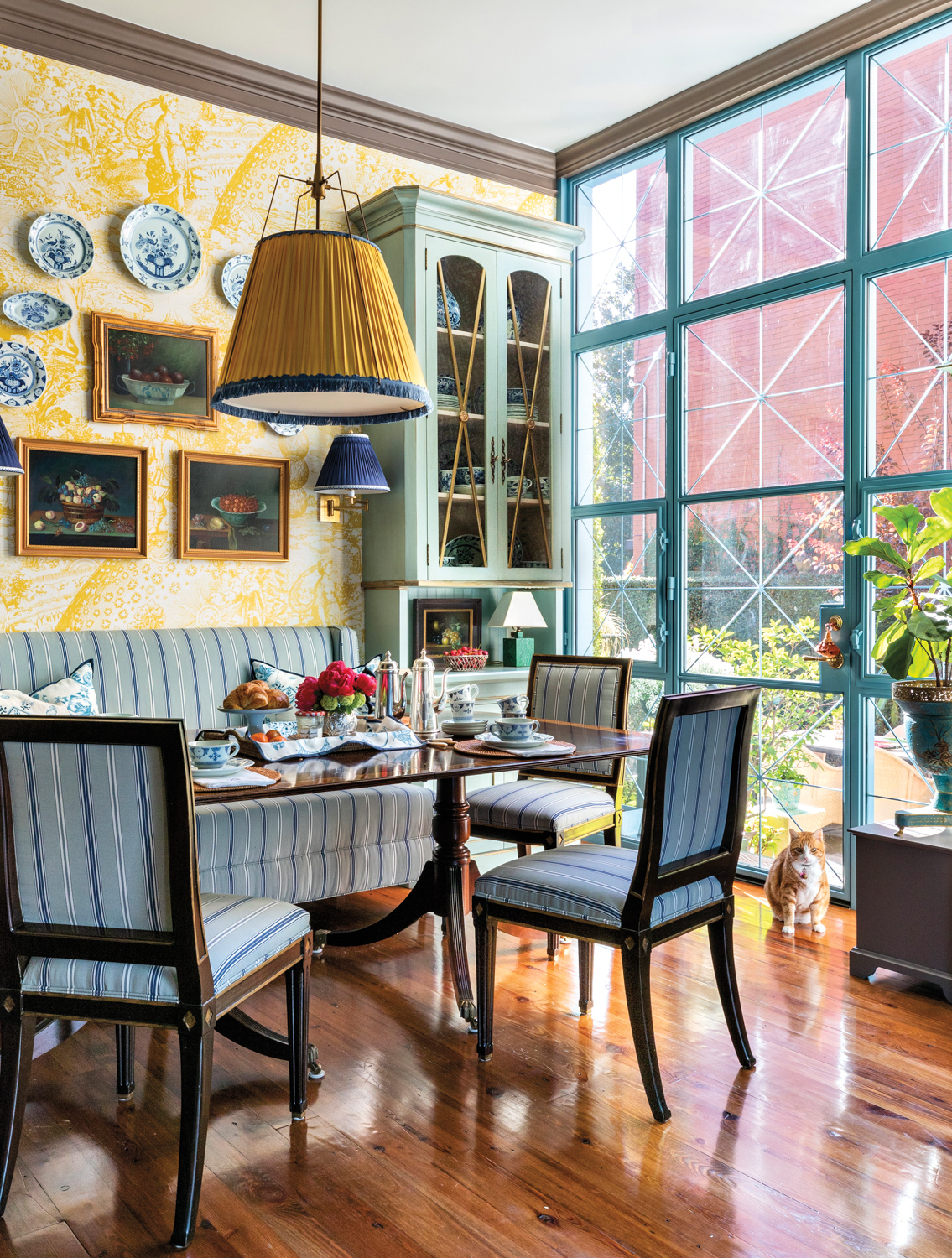 Breakfast room with yellow toile wallpaper, blue upholstery on the banquette and dining chairs, and blue paint on the built-in cabinetry
