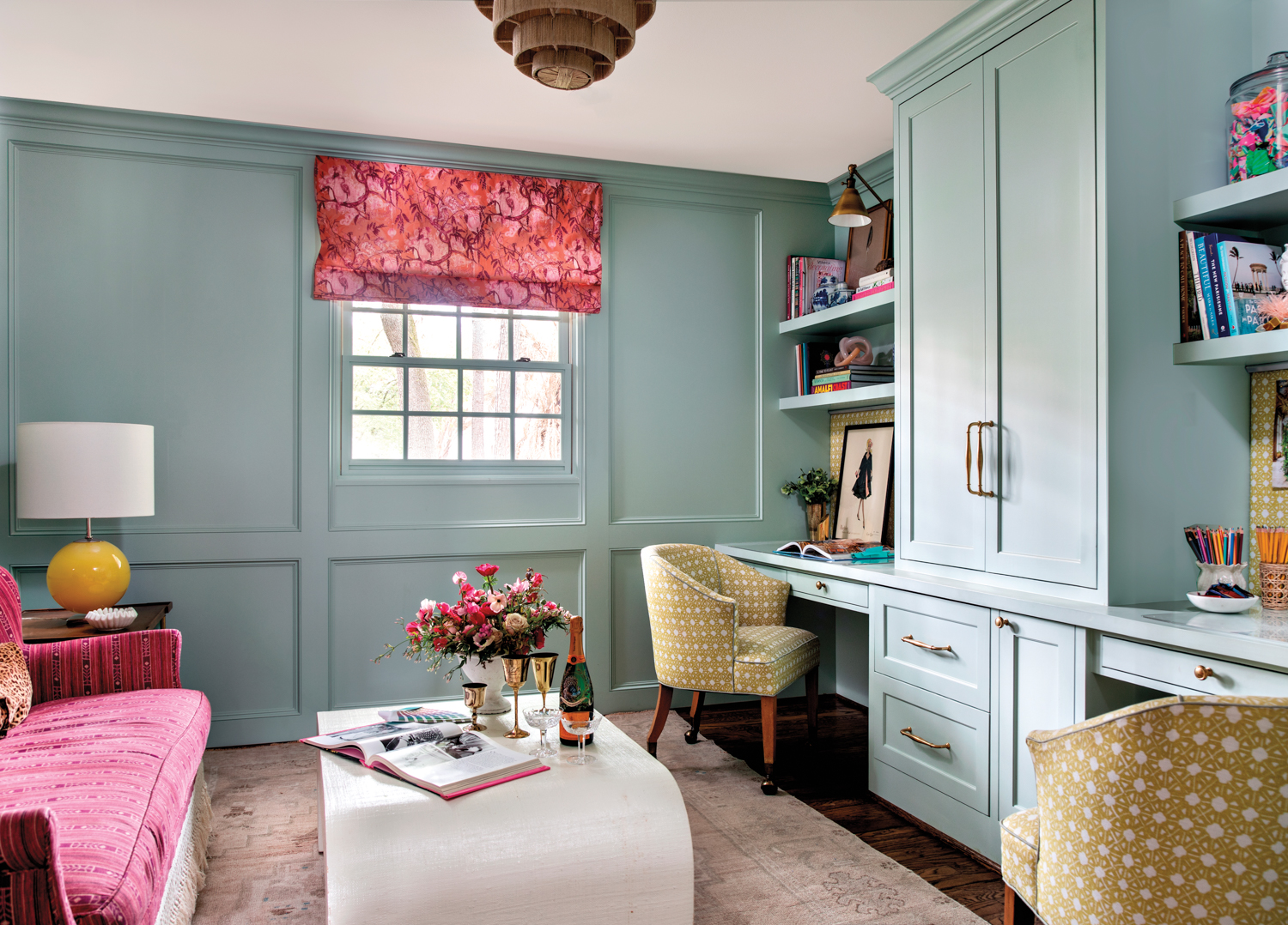 An intimate office featuring blue-painted walls, a pink sofa, an oversize coffee table and a large cabinet for storage.