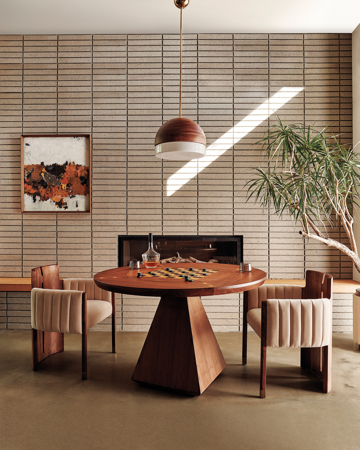Geometric wood dining table with two chairs by Lawson-Fenning for CB2 on display in front of a textured wall and fireplace