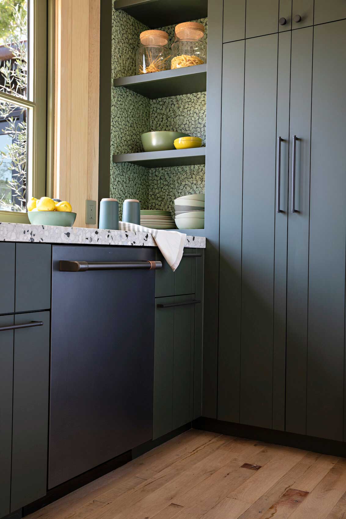 kitchen vignette with dark green cabinetry, green patterned wallpaper and terrazzo countertops