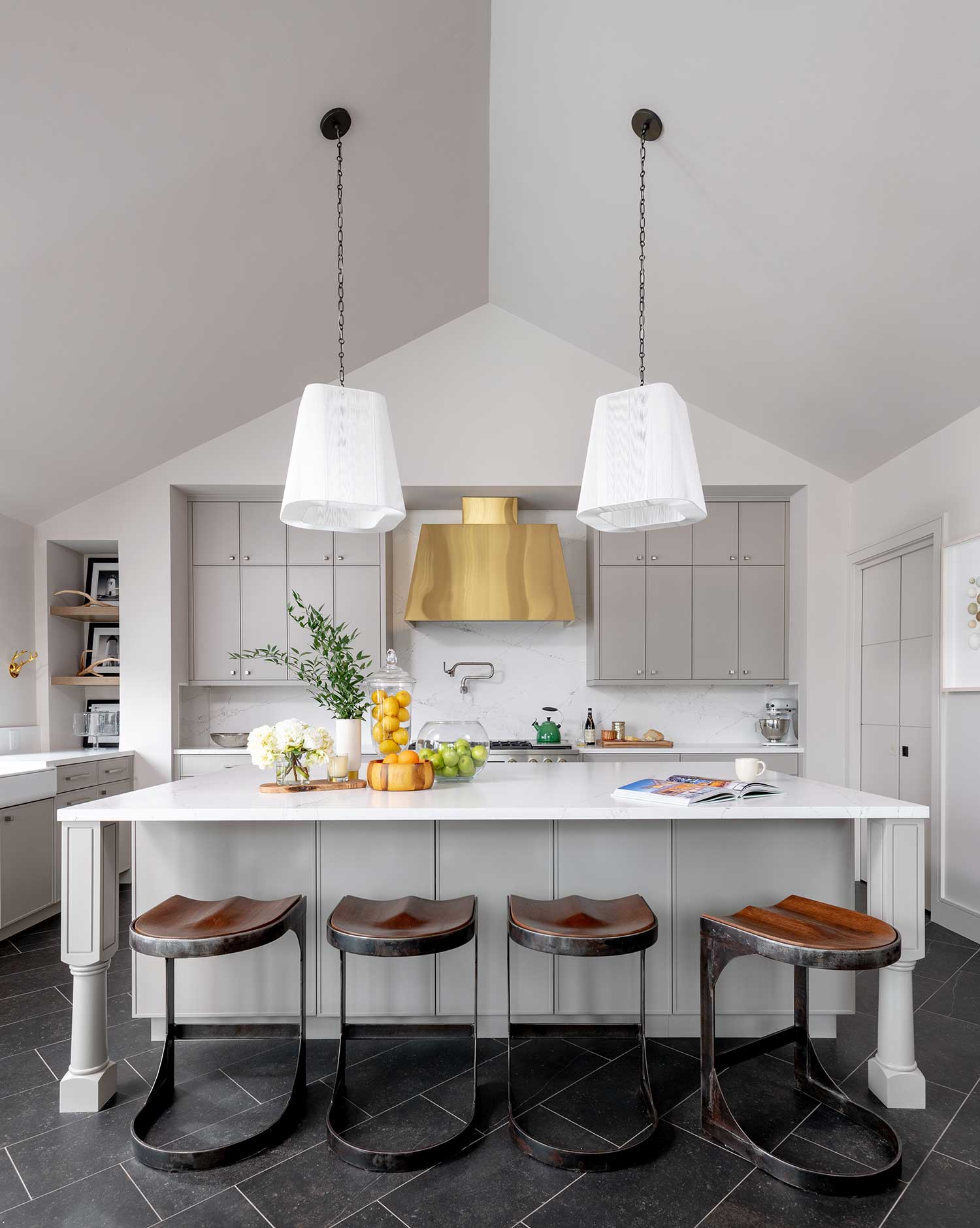 kitchen with white ceiling, gray cabinetry, black tile flooring, gold range hood, wood stools and white pendants