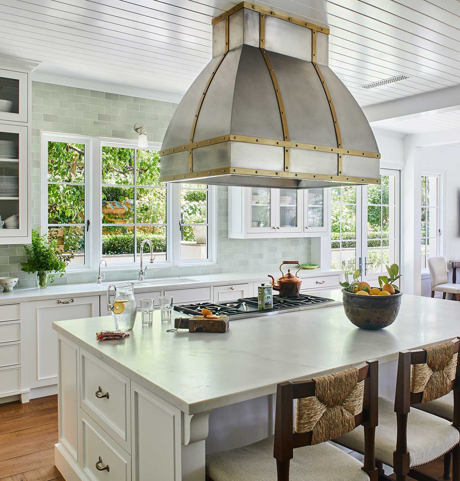 kitchen with large metal hood over island, light green tile backsplash and wood counter stools