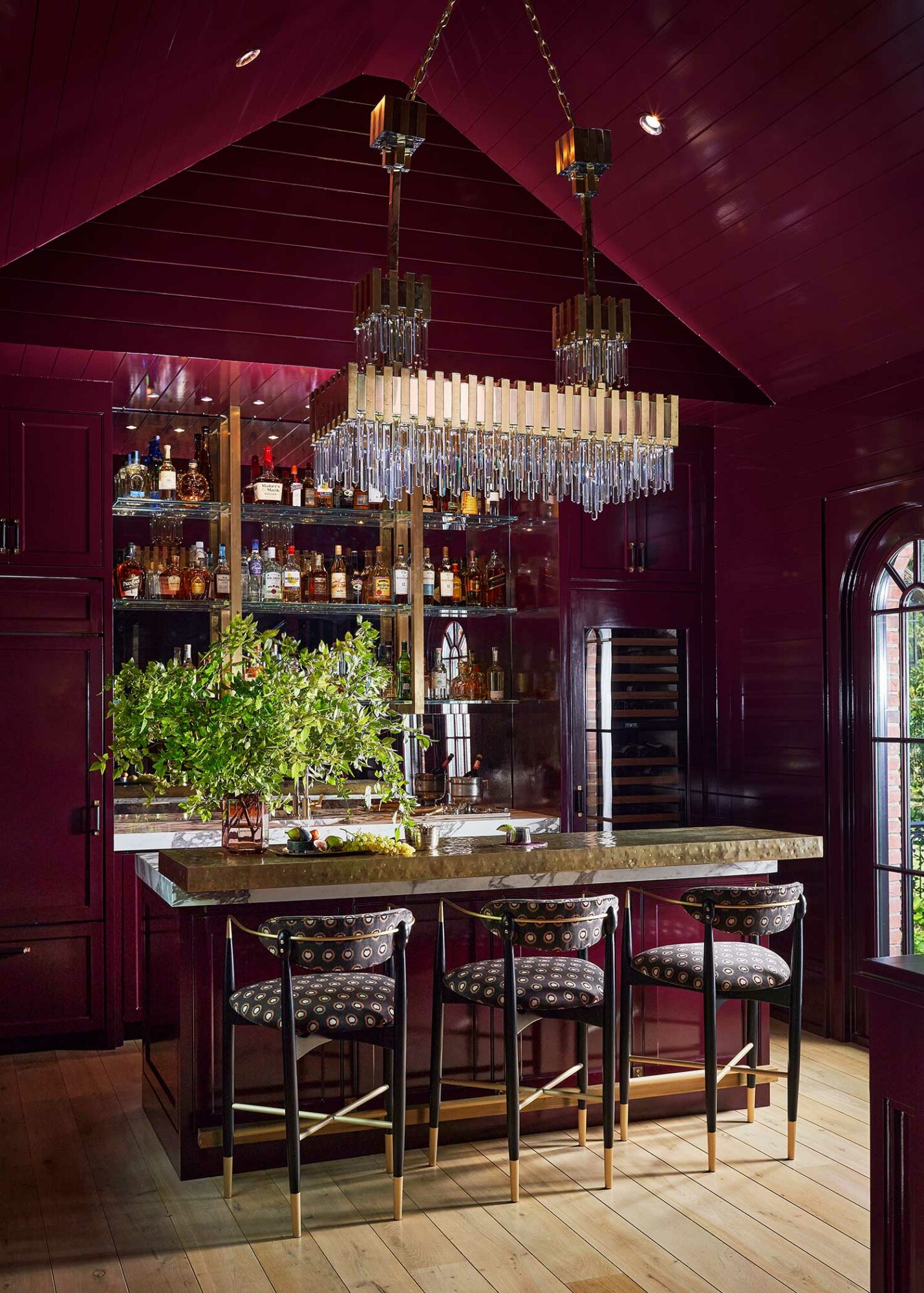 bar area painted glossy maroon with crystal chandelier hanging from peaked ceiling and three counter stools