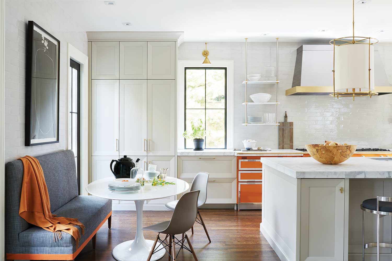 white kitchen with orange range, gold accents, blue banquette, white tulip table and two white chairs