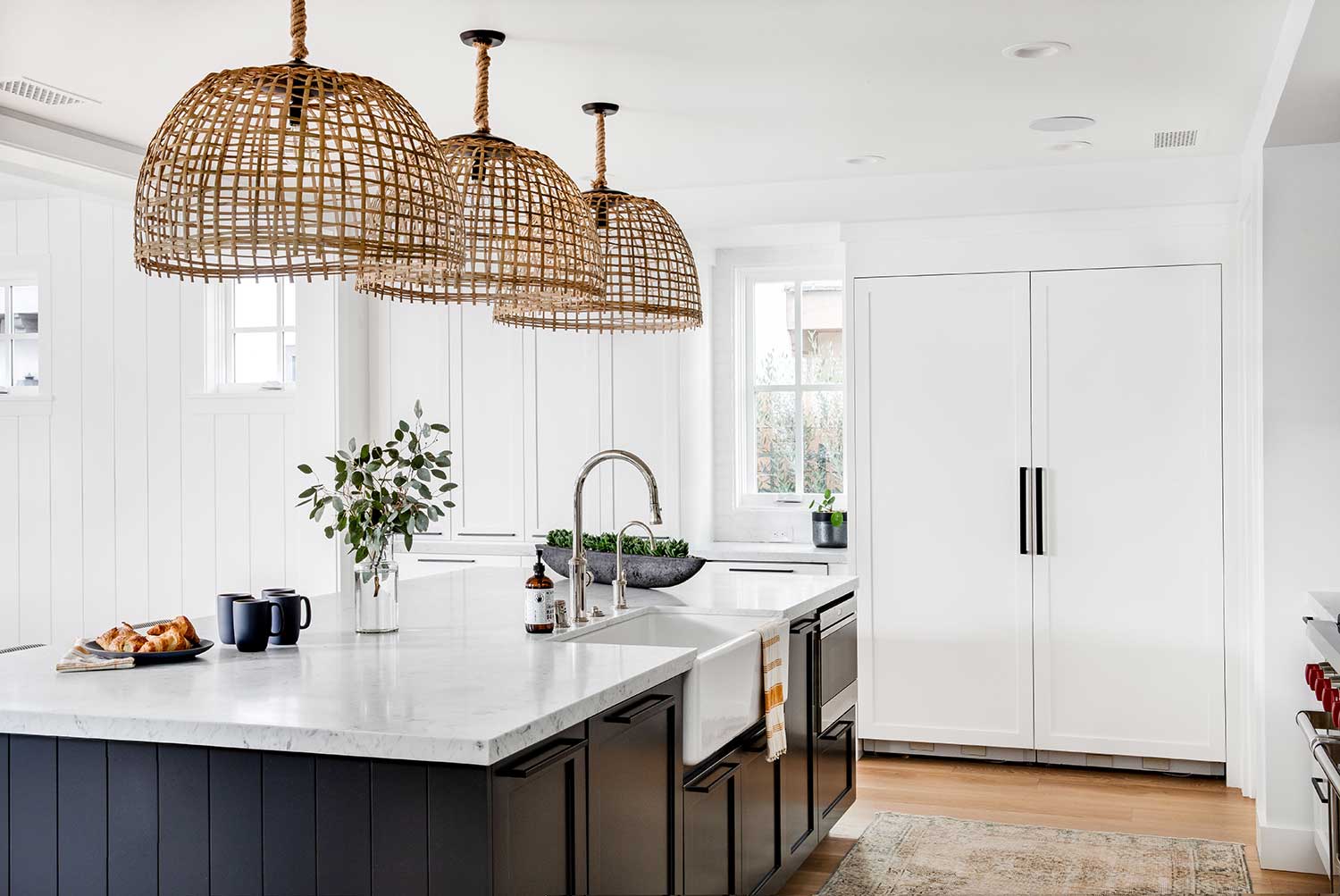 white kitchen with navy island and three oversize rattan lighting pendants
