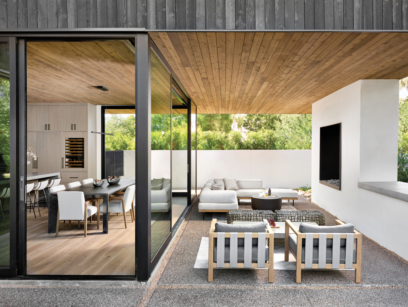 The patio outside the dining room, which has a collection of gray seating. Floor-to-ceiling glass doors open to blend the indoors and outdoors.