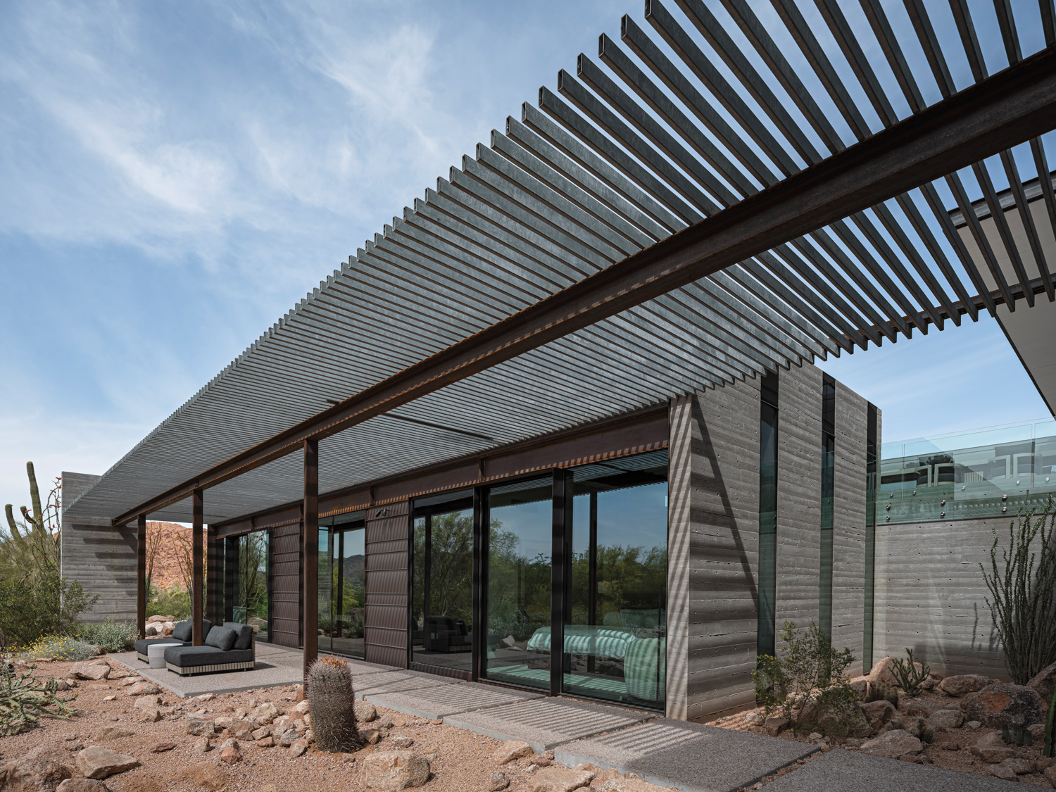 A steel-beam trellis hangs over the patio of a modern home.