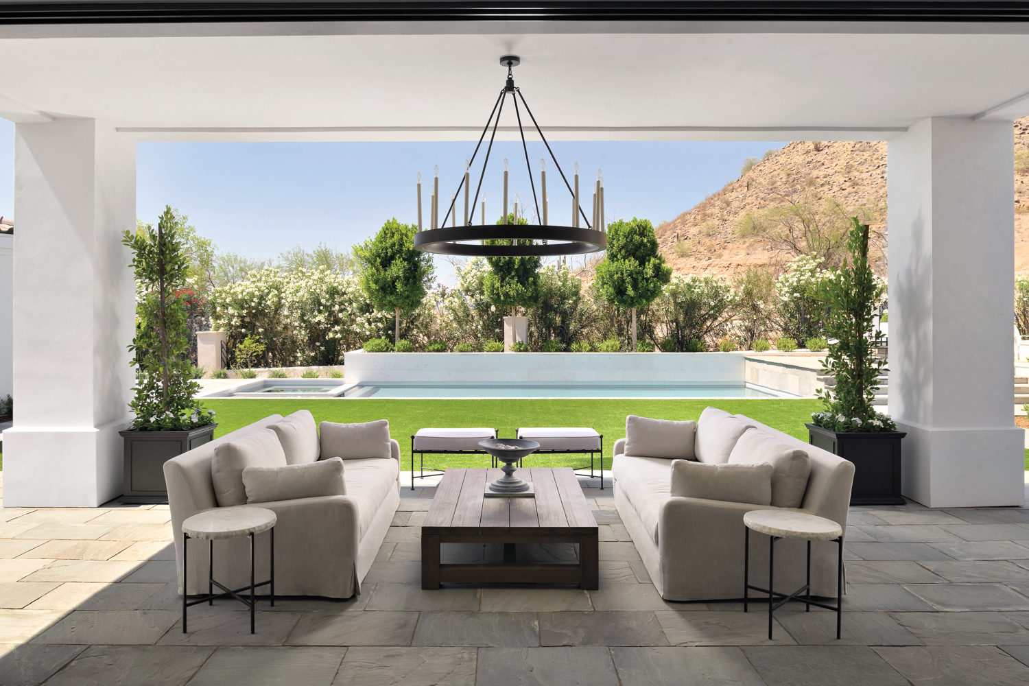 An outdoor stone patio overlooking a pool with two white couches and a coffee table.