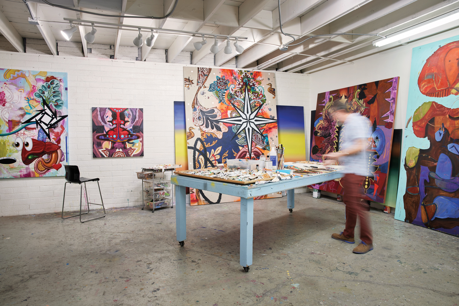 An artist in a large studio with large, colorful paintings on the walls.
