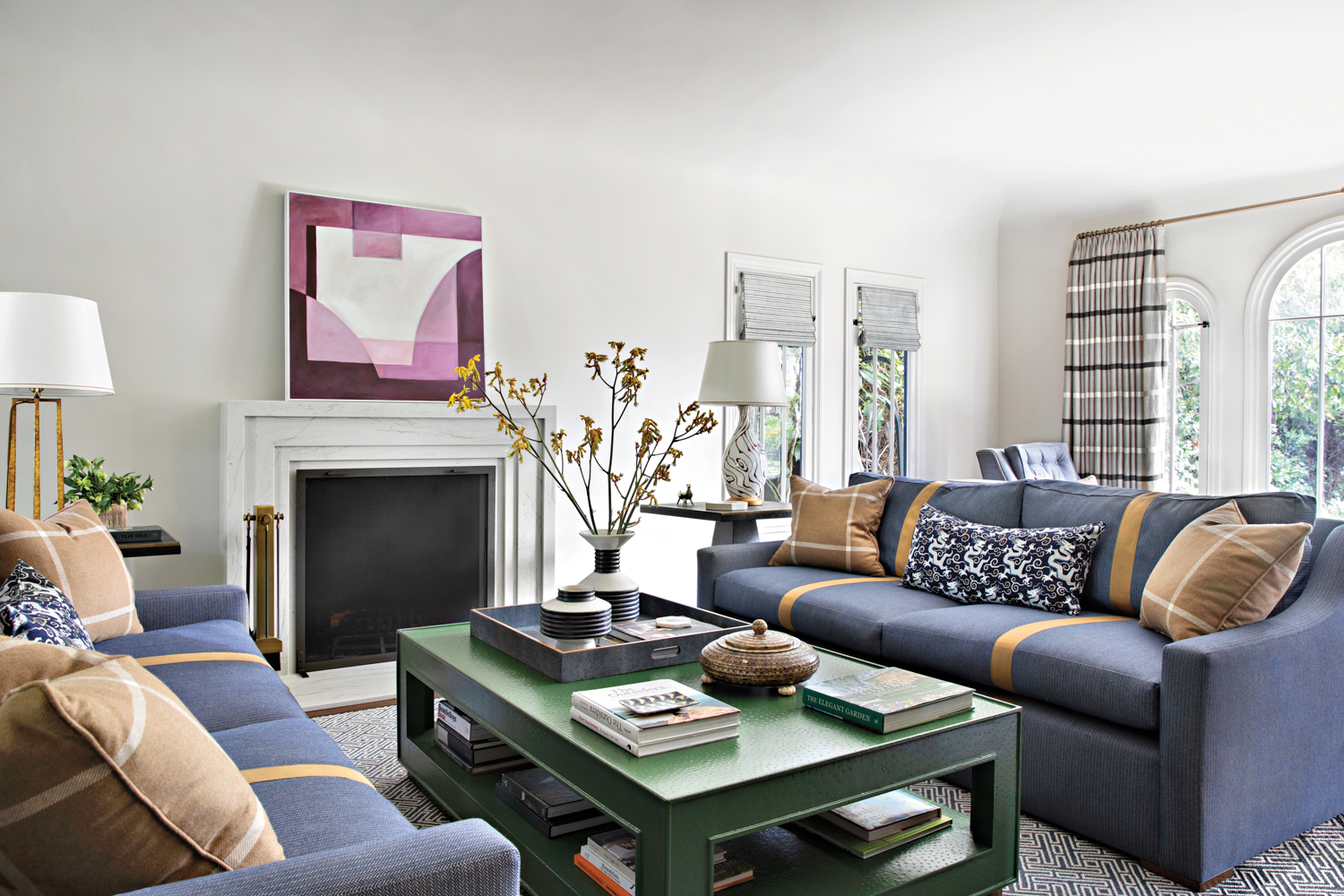 living room with twin gray fabric sofas, a green coffee table, a fireplace and white mantle with an abstract painting hung above