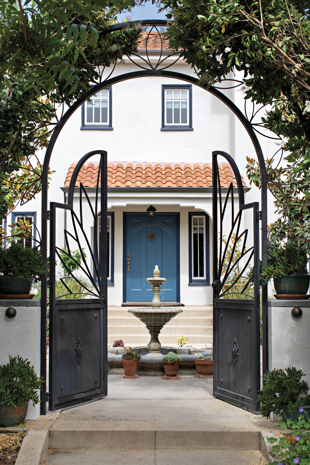 front yard of Mediterranean garden with arched iron gates, bird bath and blue front door