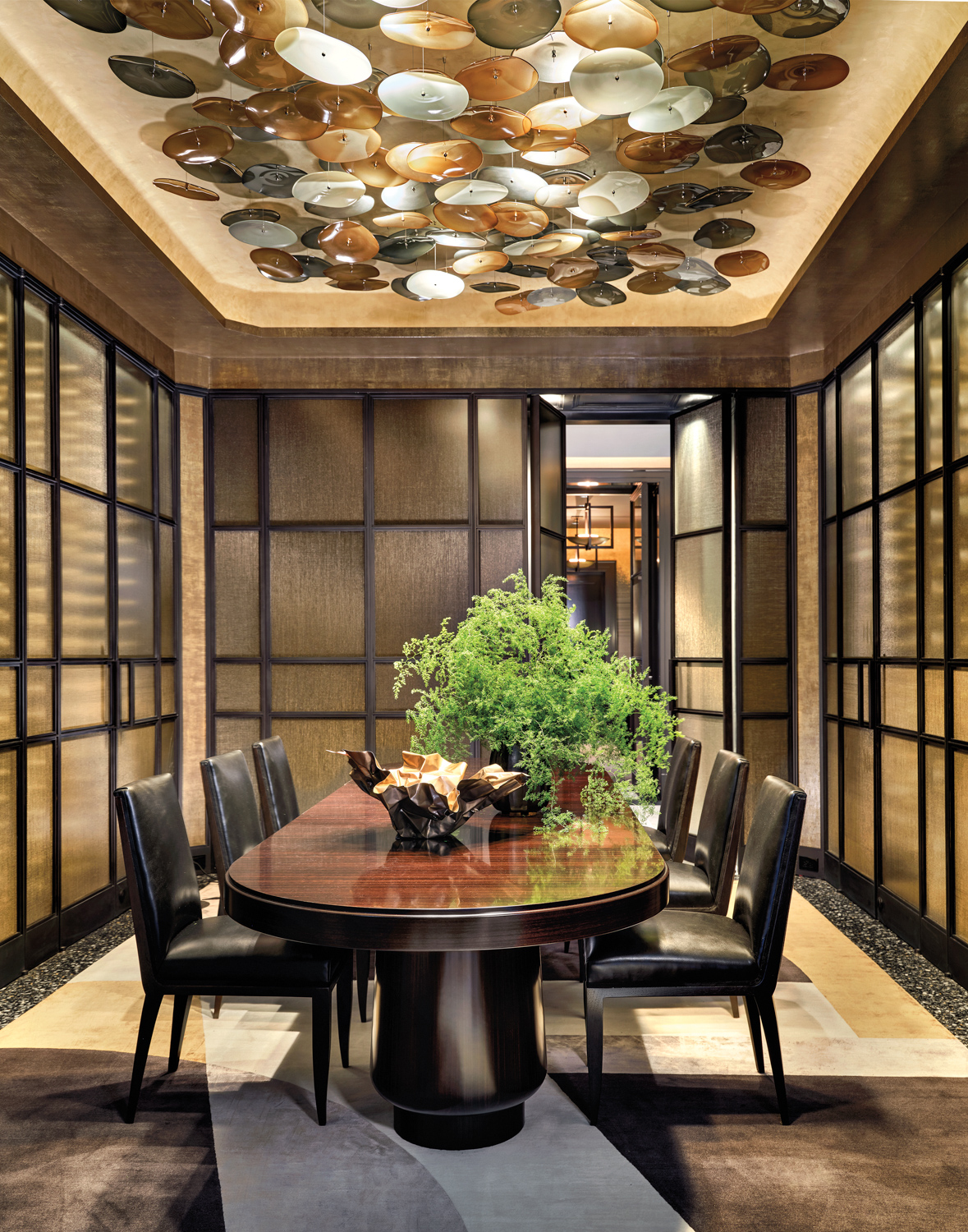 A gilded dining room with a blown-glass lighting installation above and a wine display cabinet.