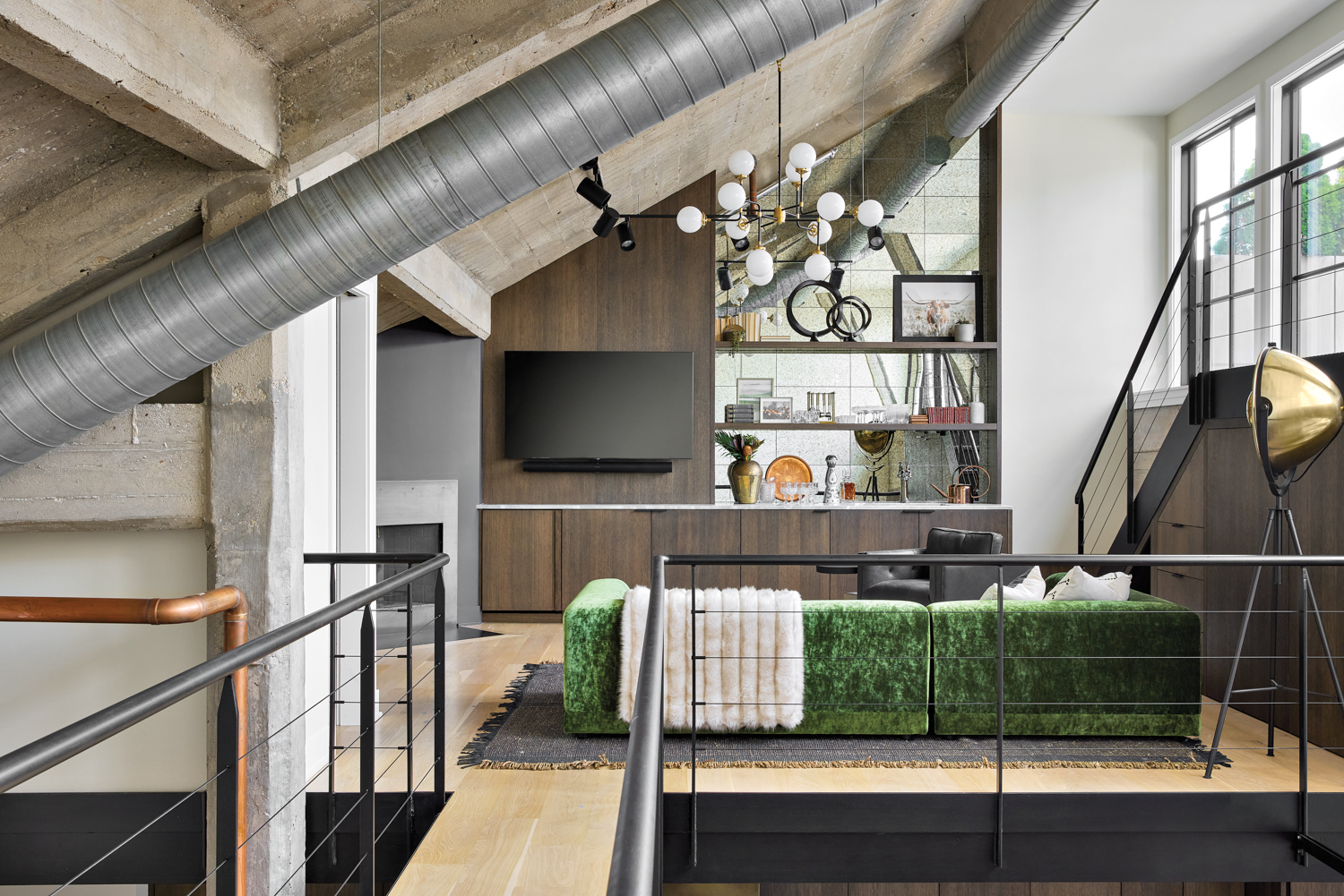 A loft living space with a green velvet sofa and exposed ductwork.
