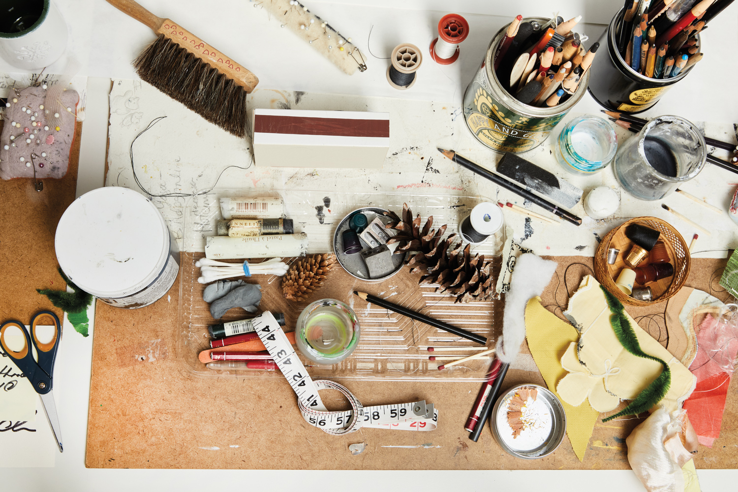 An overview of an artist's table with pencils, embroidery thread, a measuring tape and other art supplies.