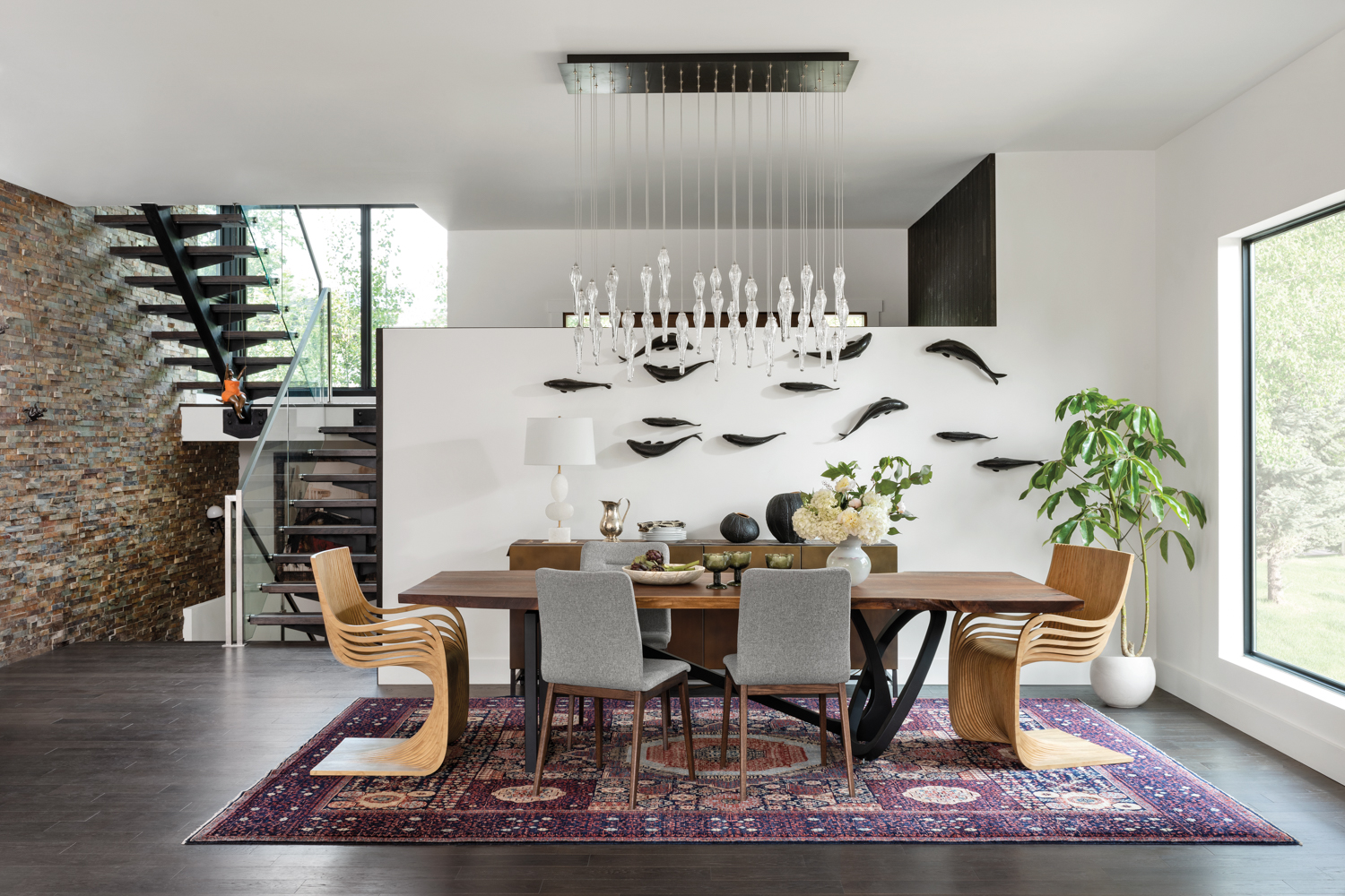 dining table and chairs below a spear pendant installation and bronze carp artwork on the wall