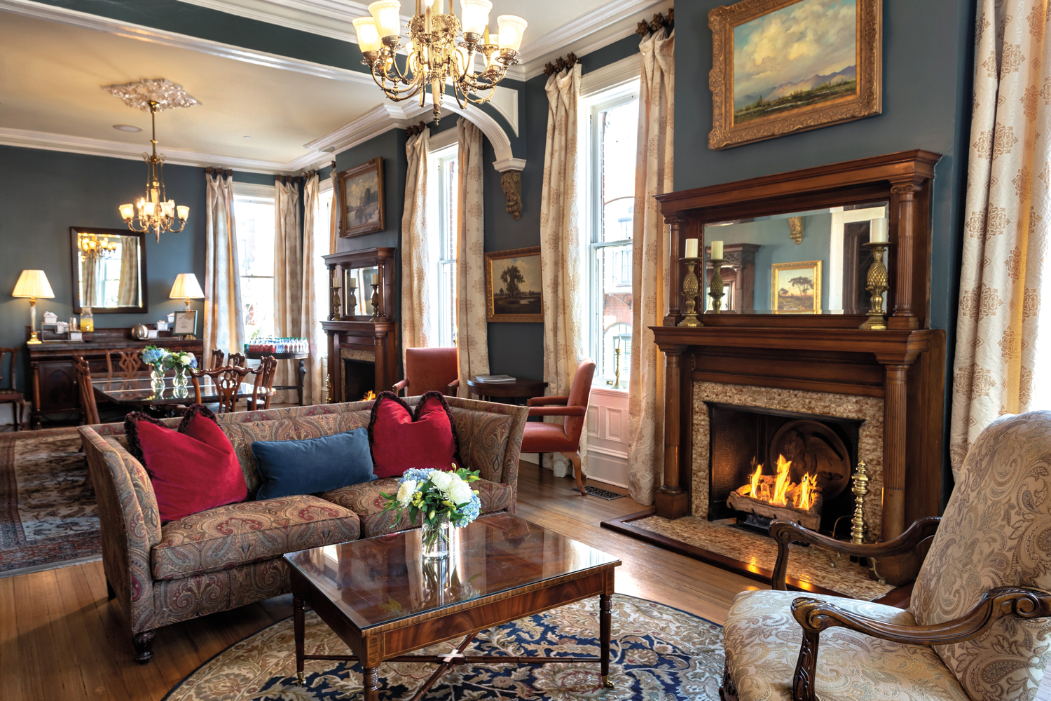 Historic great room with dining and seating areas, a fireplace and several large windows