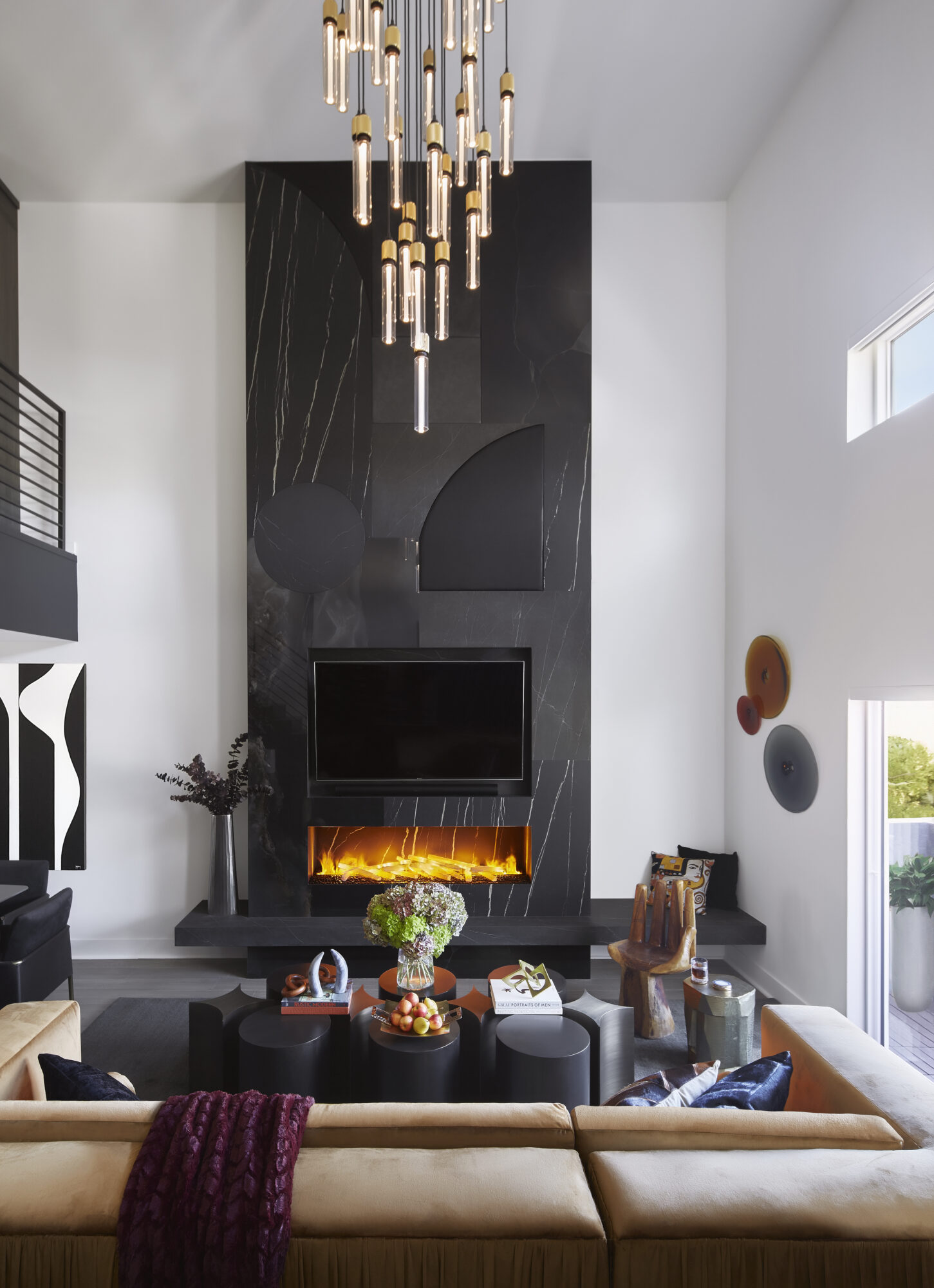 living room with black fireplace surround stretching up to ceiling, long chandelier, and tan couch