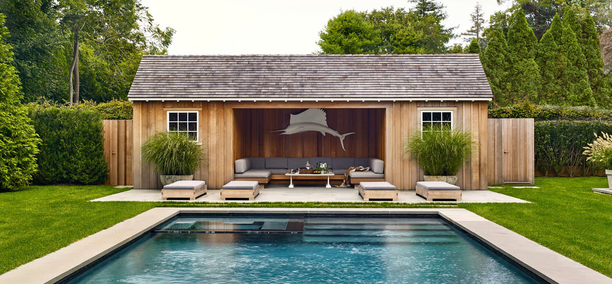 A rustic and classic Hamptons pool house with built-in banquette for entertaining outdoors