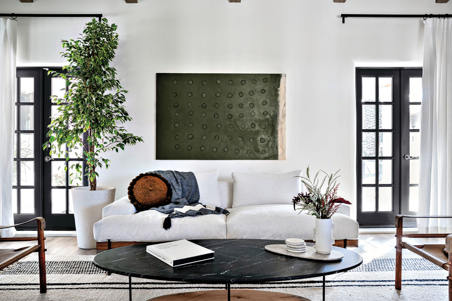 Above a white sofa hangs a deep green abstract painting. In front of it is a black-marble-and-wood coffee table.