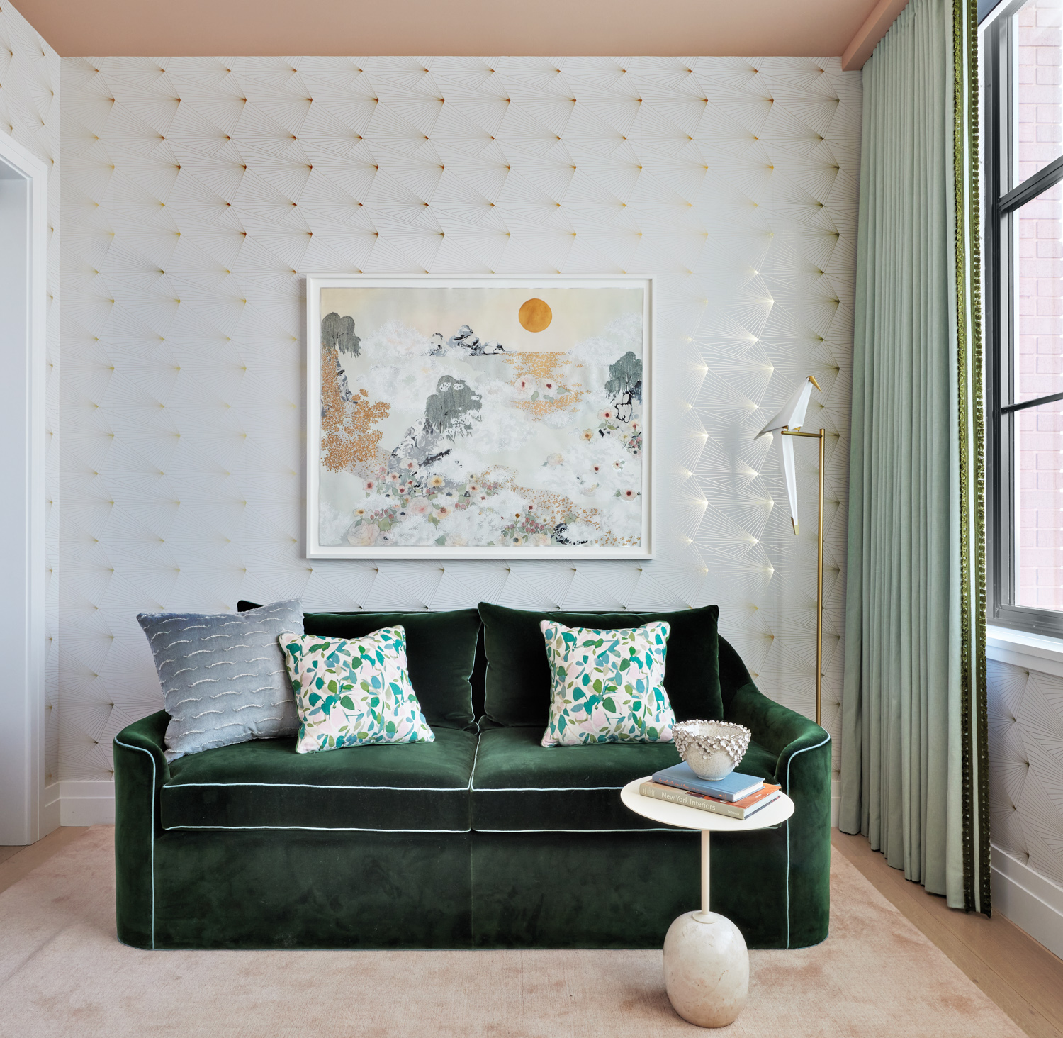 Room with a green velvet couch, a pink rug and white-and-gold foil wallpaper.