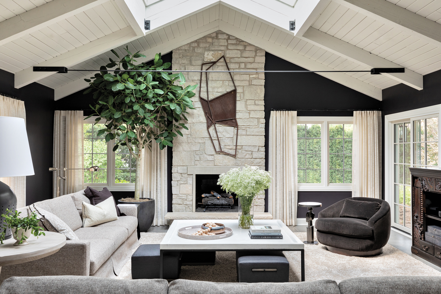 Great room with black walls, white vaulted ceiling, gray upholstered furnishings and a stone fireplace.