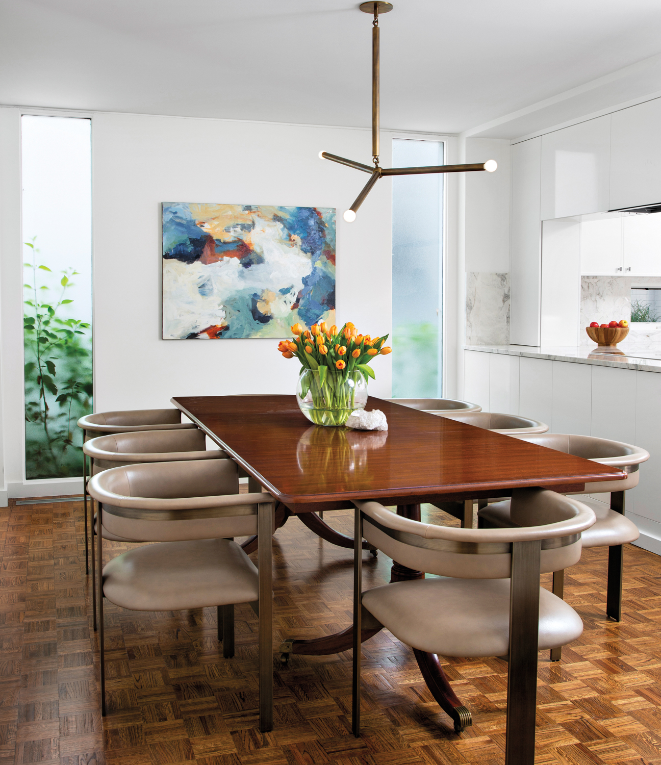 dining table with tan curved chairs and contemporary chandelier with abstract art on wall