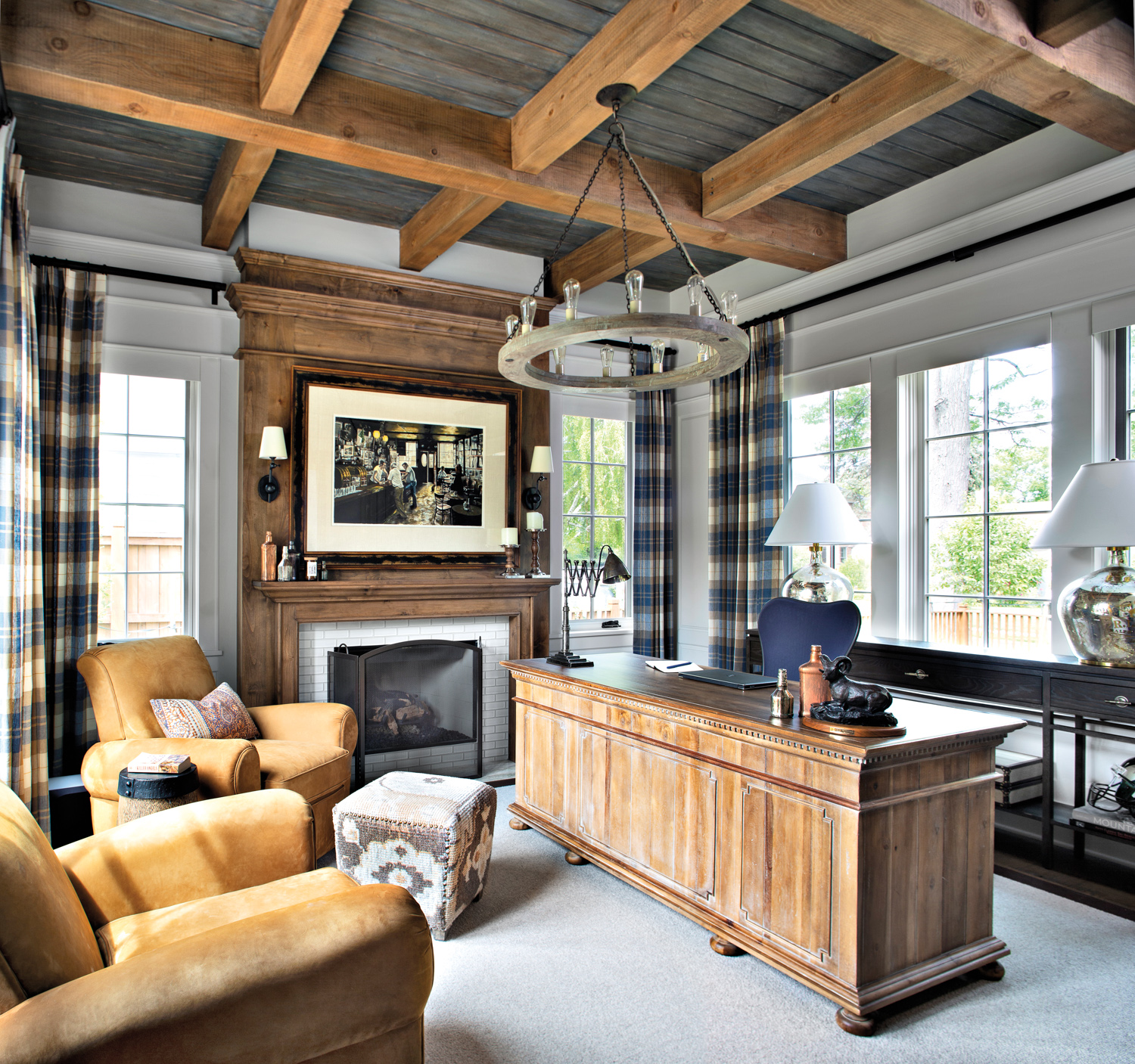 office with exposed ceiling beams, desk and armchairs, with plaid curtains and wood surround fireplace